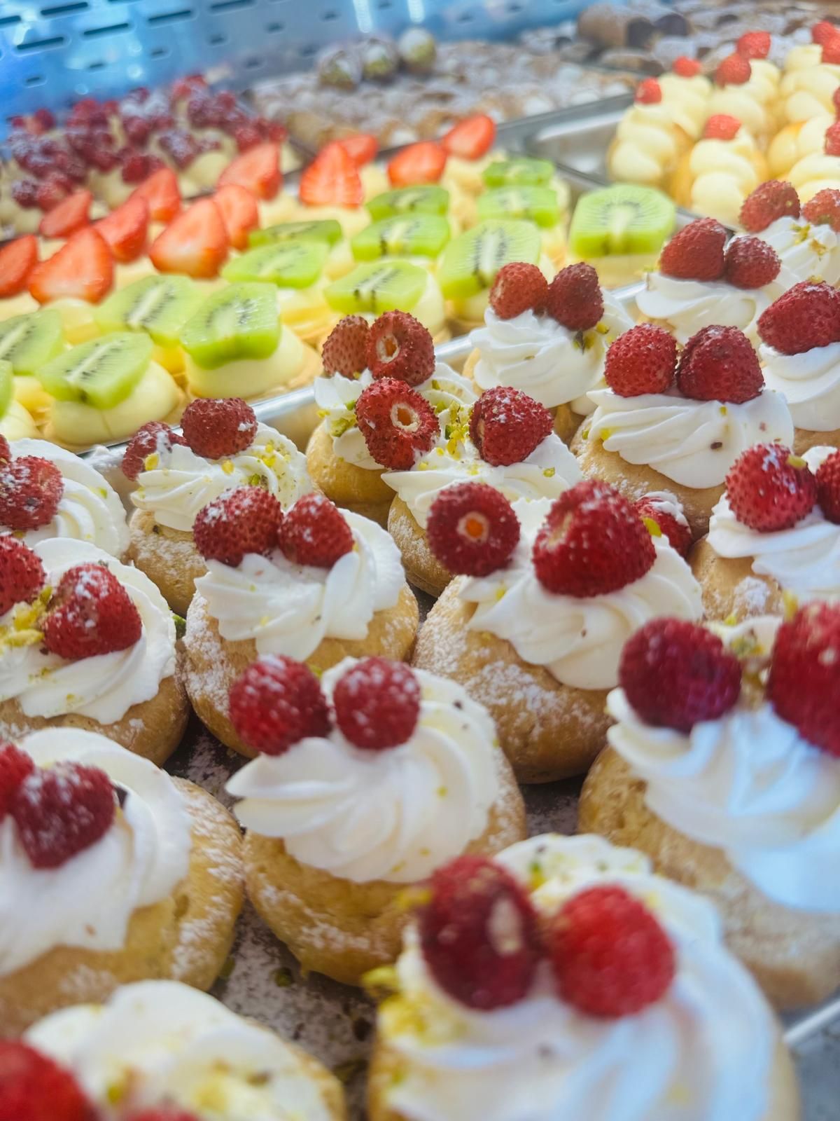 Pasticcini ricoperti di panna montata e frutti di bosco; altre crostate di frutta sullo sfondo.