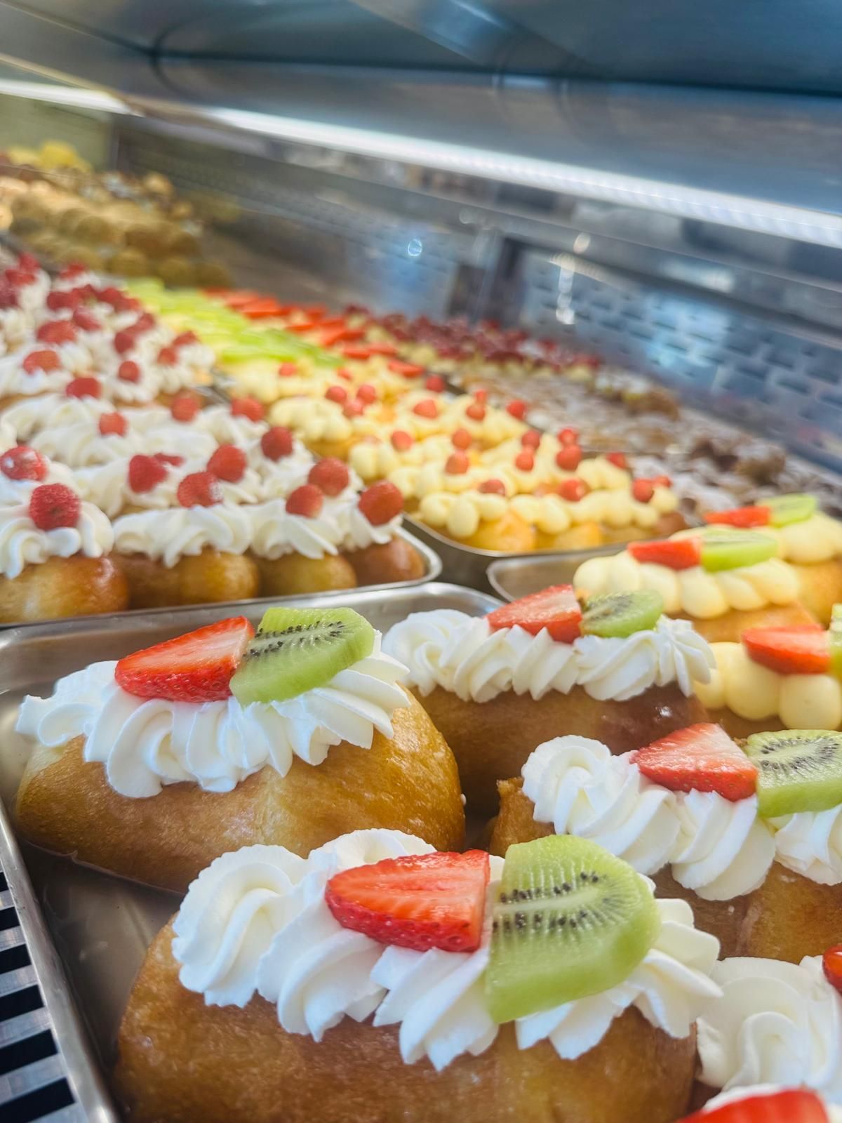 Vetrina piena di pasticcini guarniti con panna montata, fragole, kiwi e lamponi.