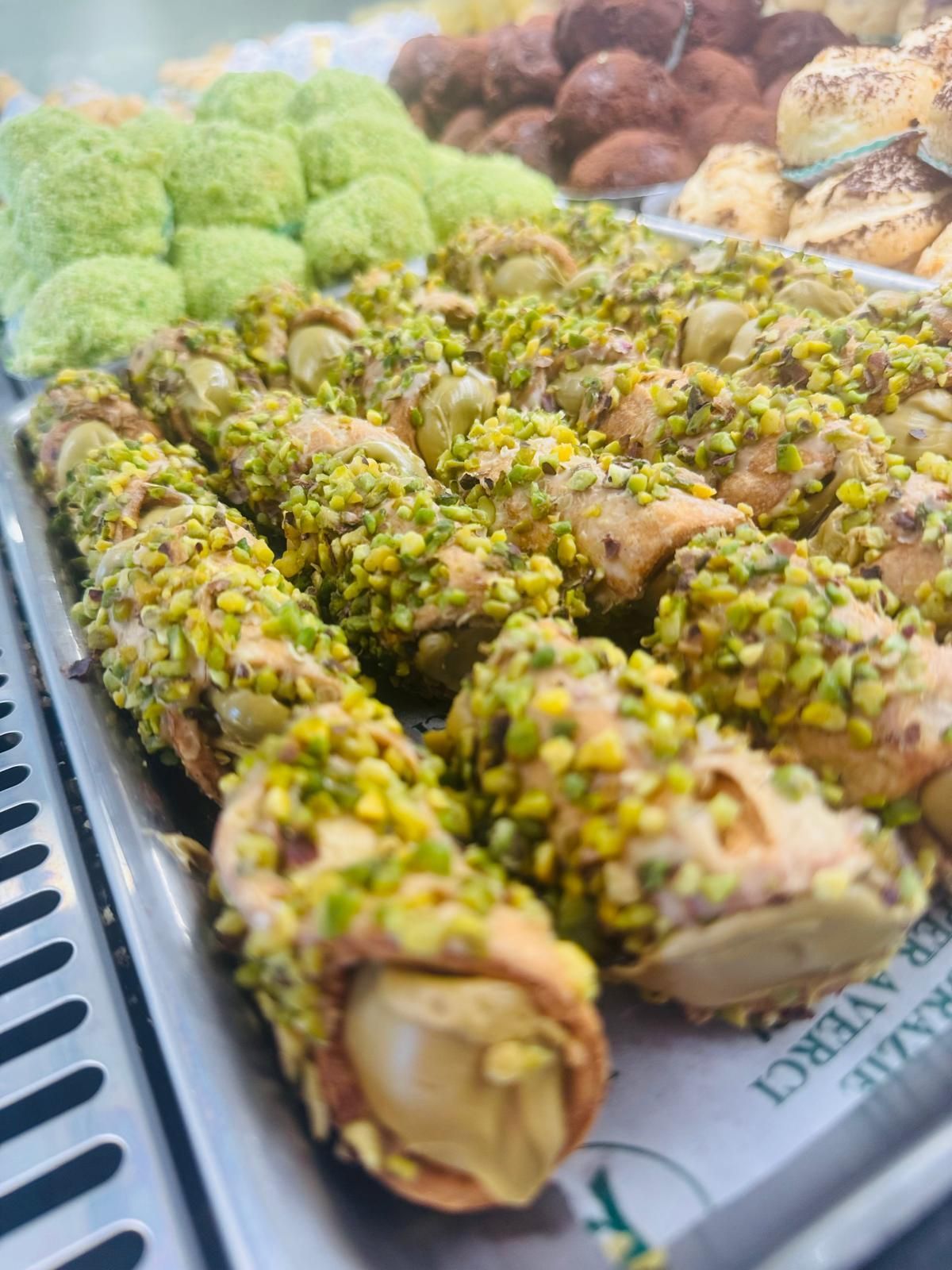 Primo piano di cannoli con guarnizione al pistacchio, esposti in una vetrina da pasticceria.