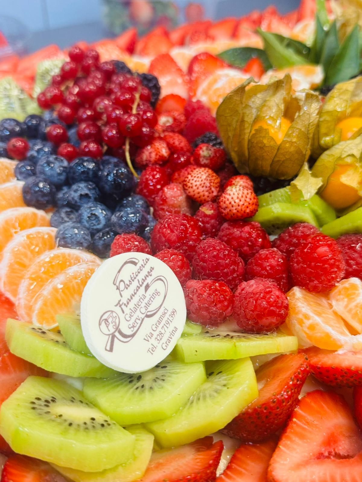 Piatto di frutta colorato con fragole, kiwi, lamponi, mirtilli, arance e altri frutti di bosco.