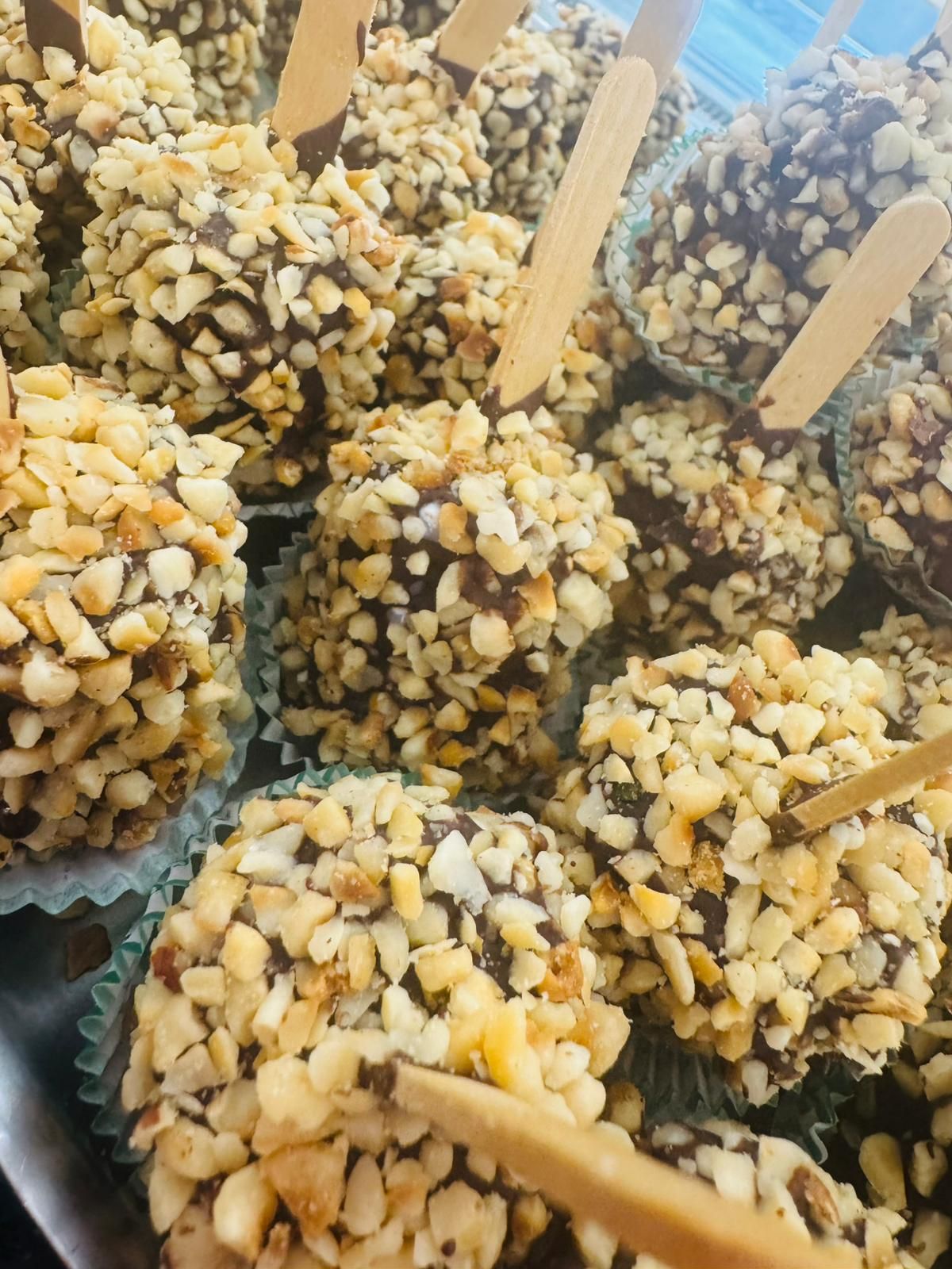 Dolcetti ricoperti di cioccolato con noci tritate, su stecchi, in bicchieri di carta.
