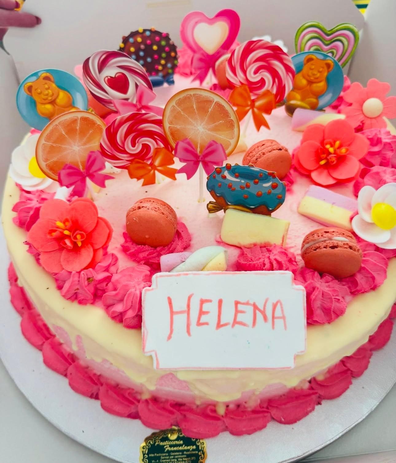 Una torta a forma di cuore con glassa rosa, decorazioni di caramelle e il nome