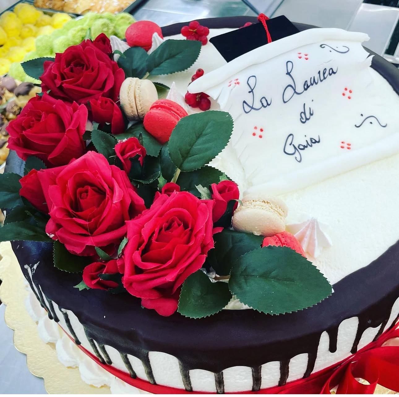 Torta decorata con rose rosse, macaron e un annuncio di laurea con la scritta