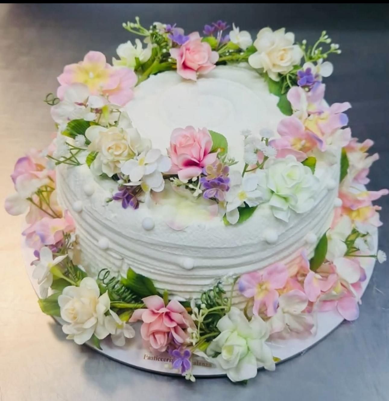 Torta bianca decorata con fiori pastello e fogliame verde.