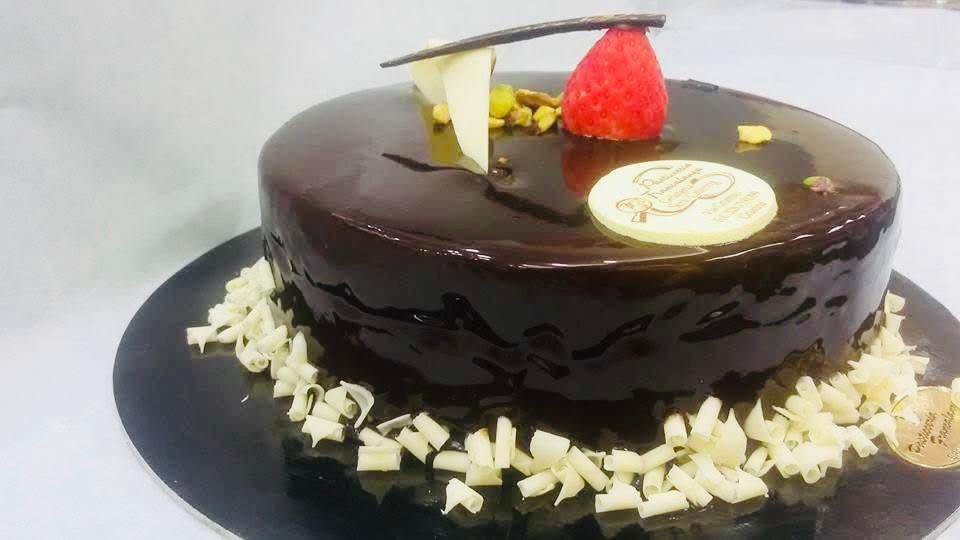 Torta al cioccolato con ganache lucida, decorata con cioccolato bianco, noci e una fragola.