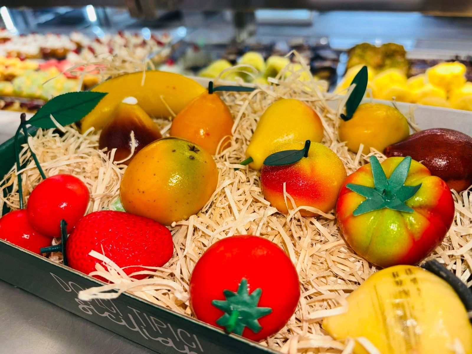 Espositore di frutta di marzapane in una scatola con cannuccia, tra cui mele, pomodori, limoni e pere.