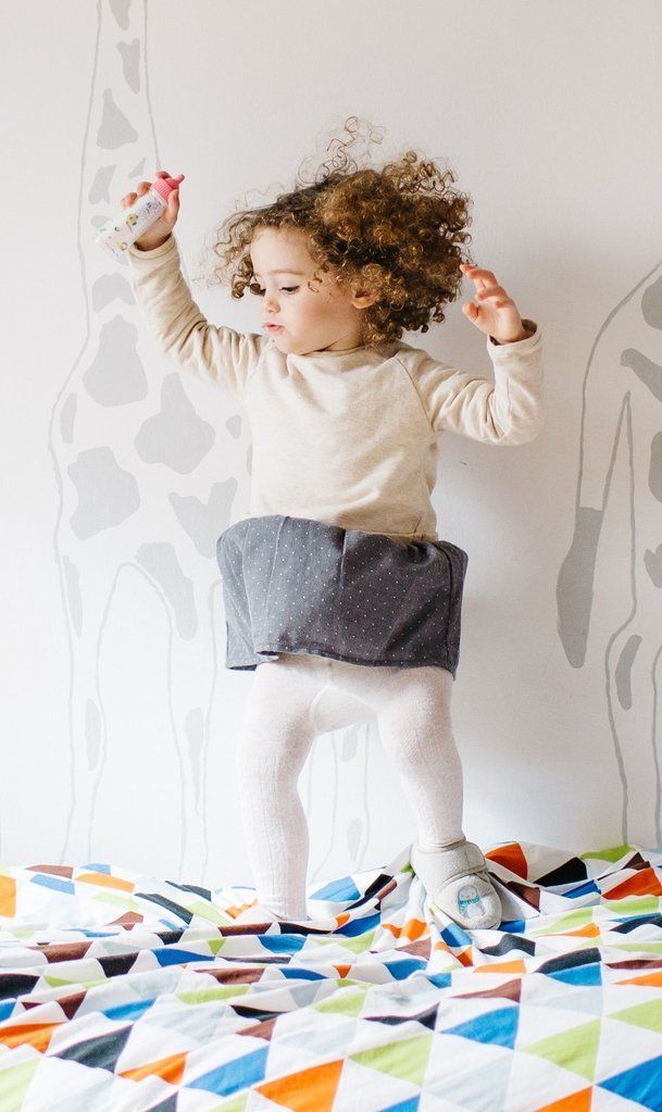 A little girl is jumping on a bed with a giraffe on the wall behind her.
