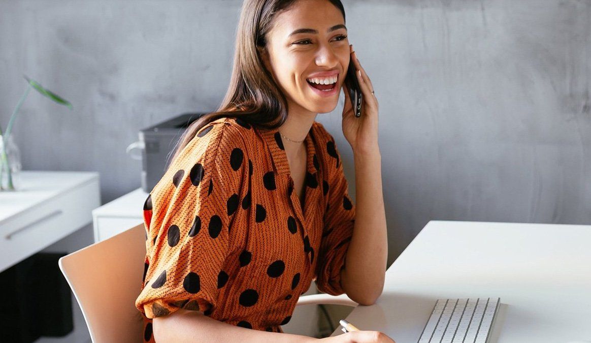 A woman is sitting at a desk talking on a cell phone.