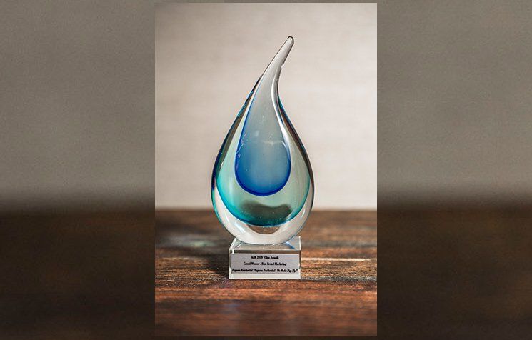 A glass sculpture of a drop of water is sitting on a wooden table.