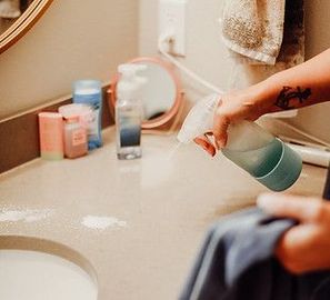 A person is cleaning a bathroom counter with a spray bottle.