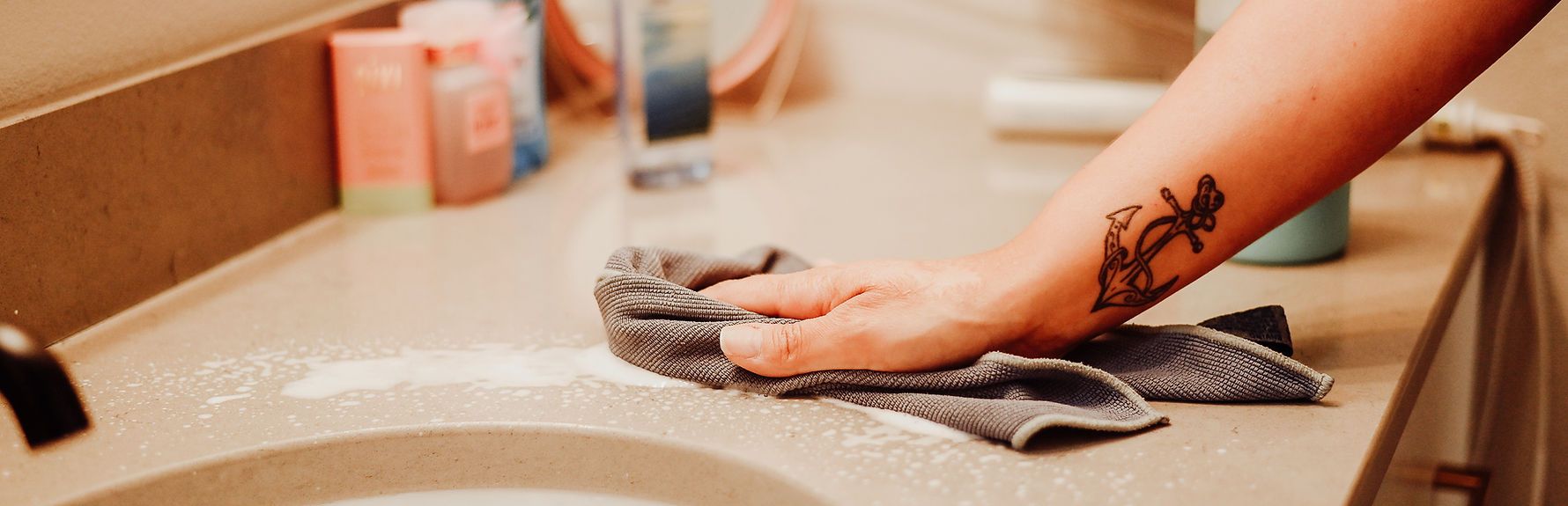 A woman is cleaning a bathroom counter with a towel.