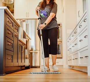 A woman is cleaning the floor in a kitchen with a mop.