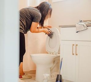 A woman is cleaning a toilet in a bathroom.