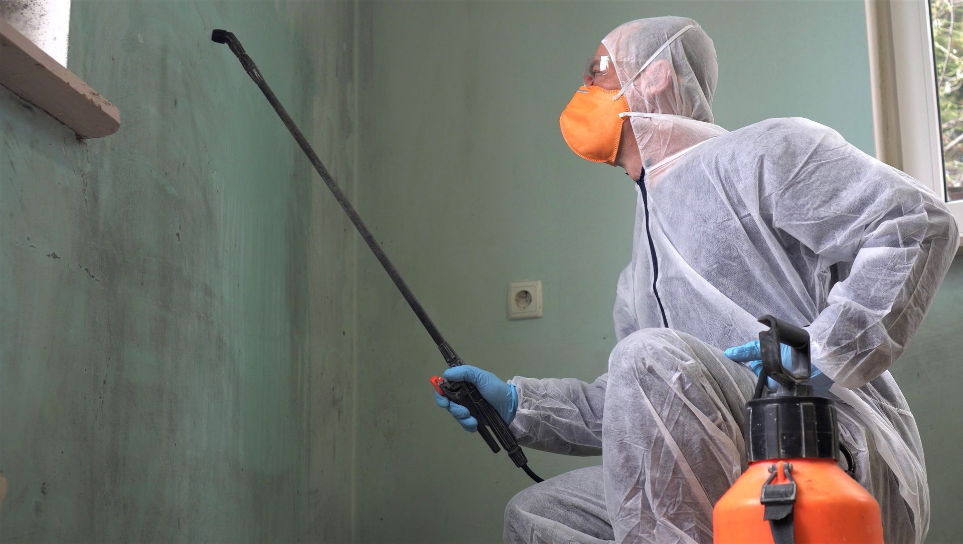 A man in a protective suit is spraying a wall with a sprayer