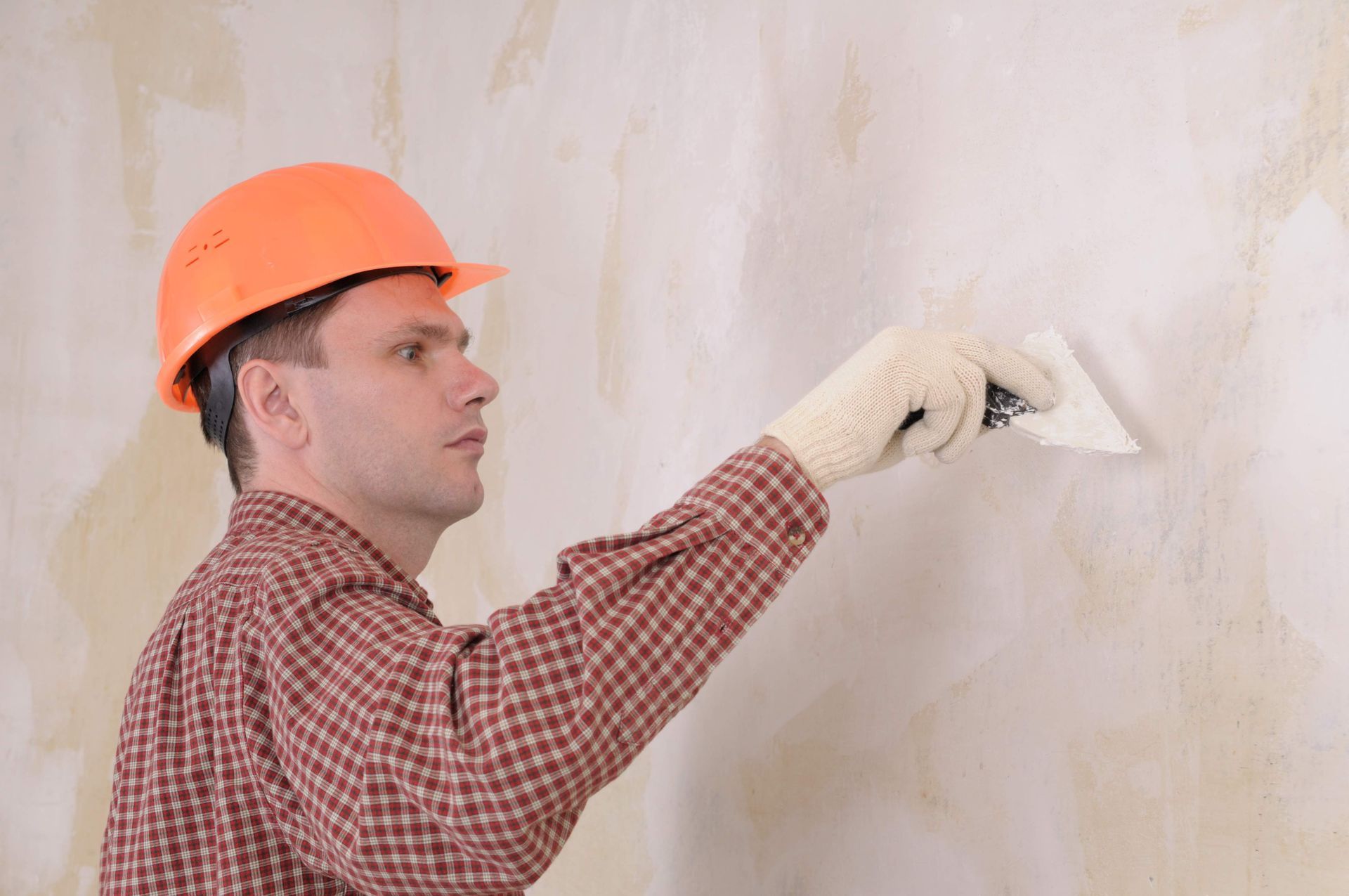 A man wearing a hard hat and gloves is plastering a wall with a spatula