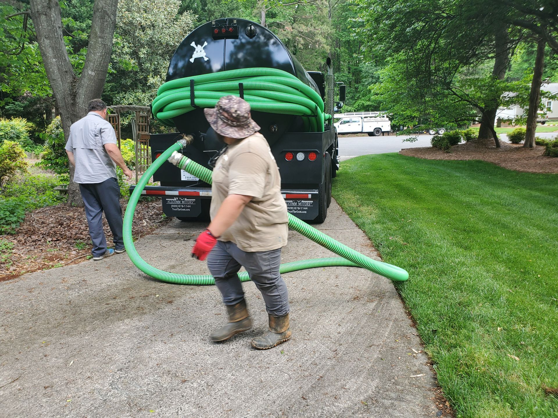 A man is standing next to a vacuum truck with a green hose attached to it