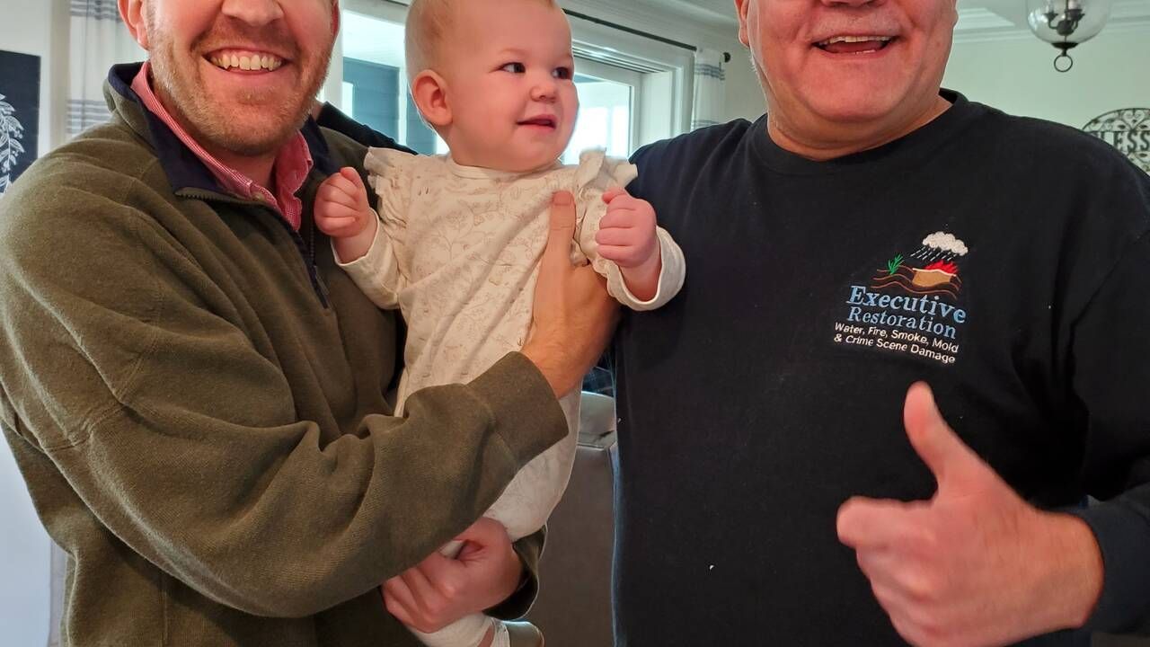 Two men are holding a baby and one is wearing a shirt that says pineapple