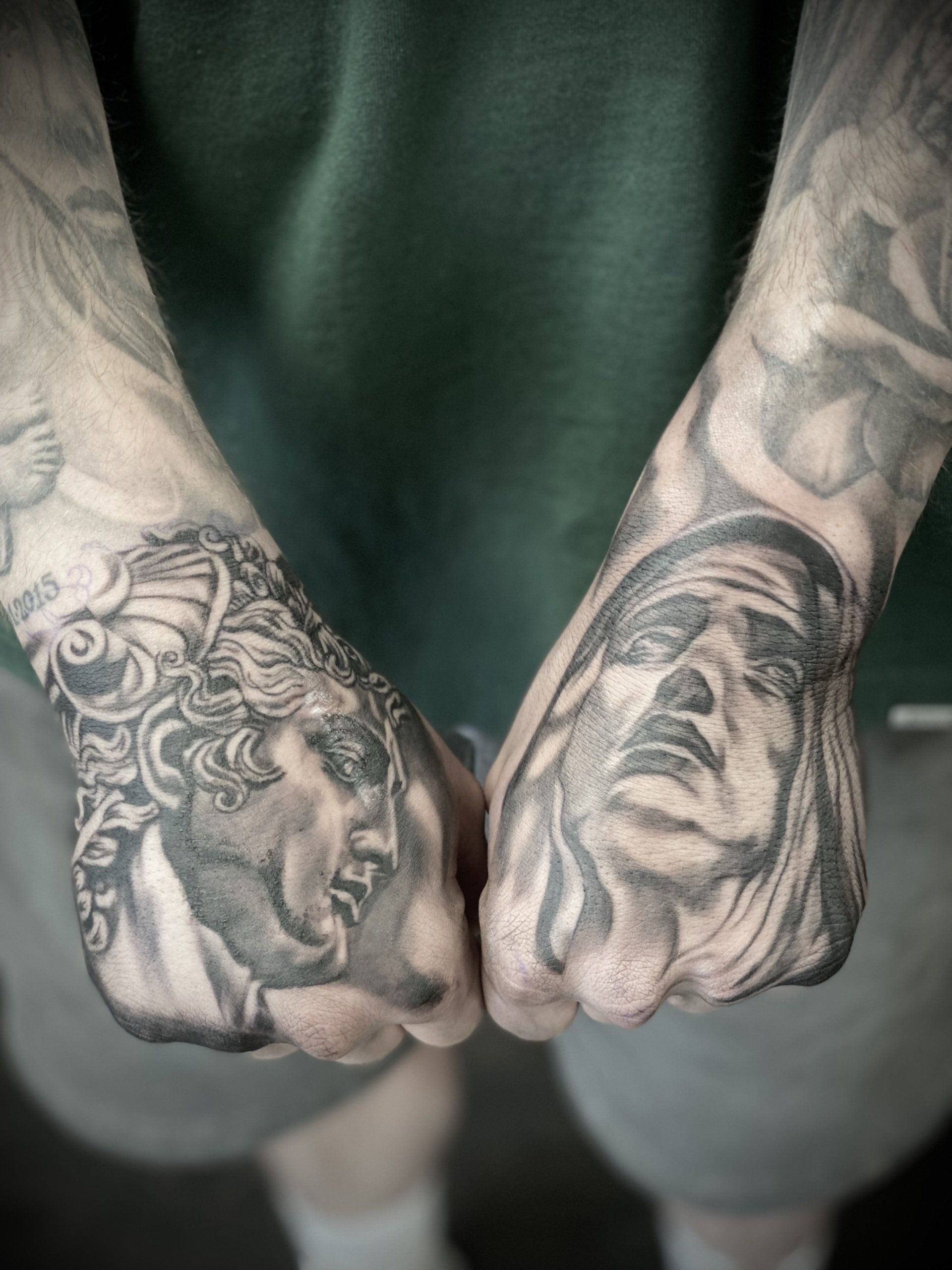 A man has two tattoos on his hands including a statue of jesus