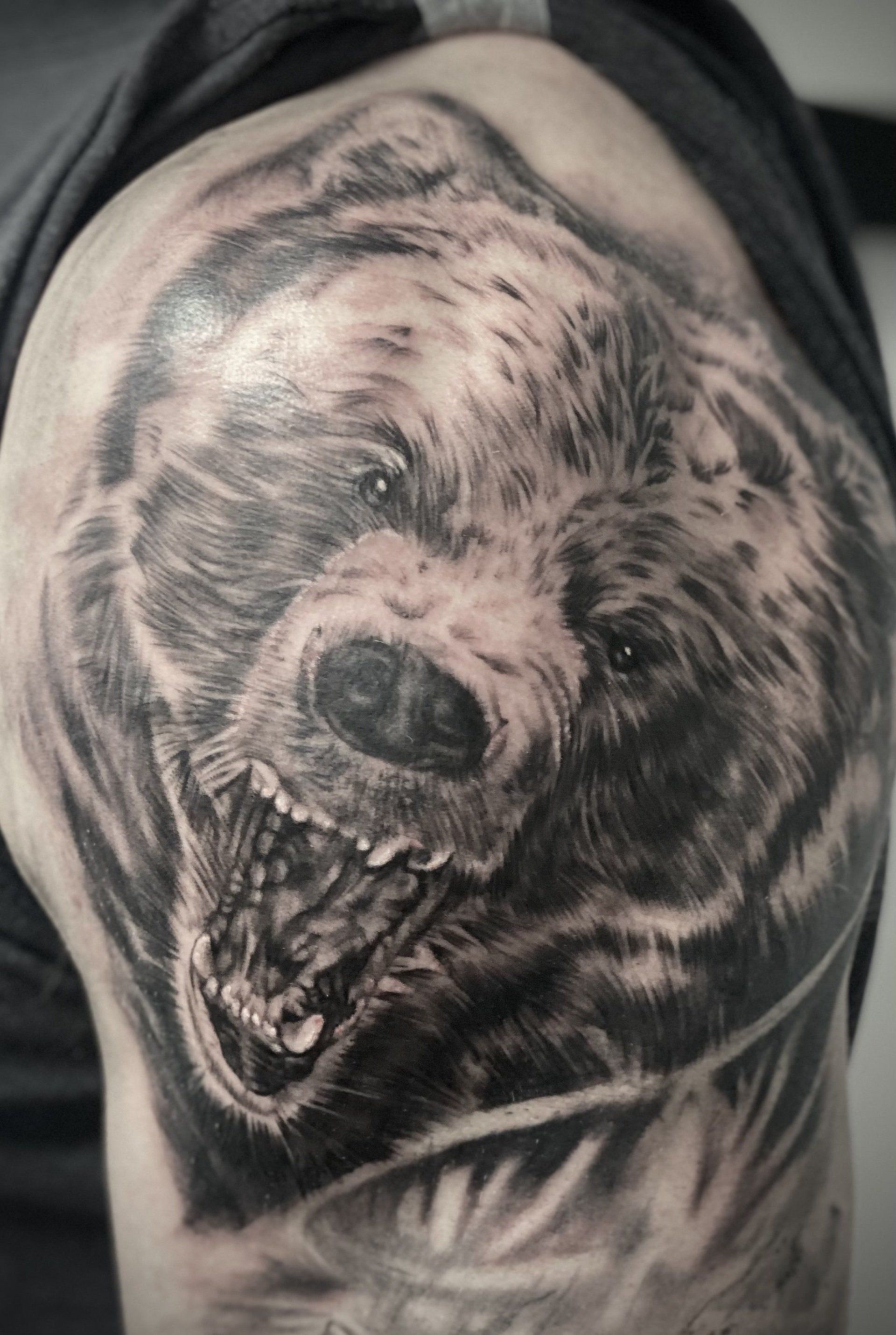 A black and white tattoo of a bear on a man 's shoulder.