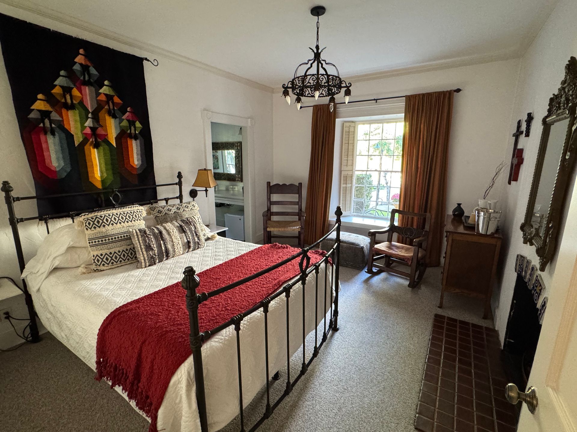Bedroom with wrought iron bed, rug, tapestry, fireplace, and window with curtains.