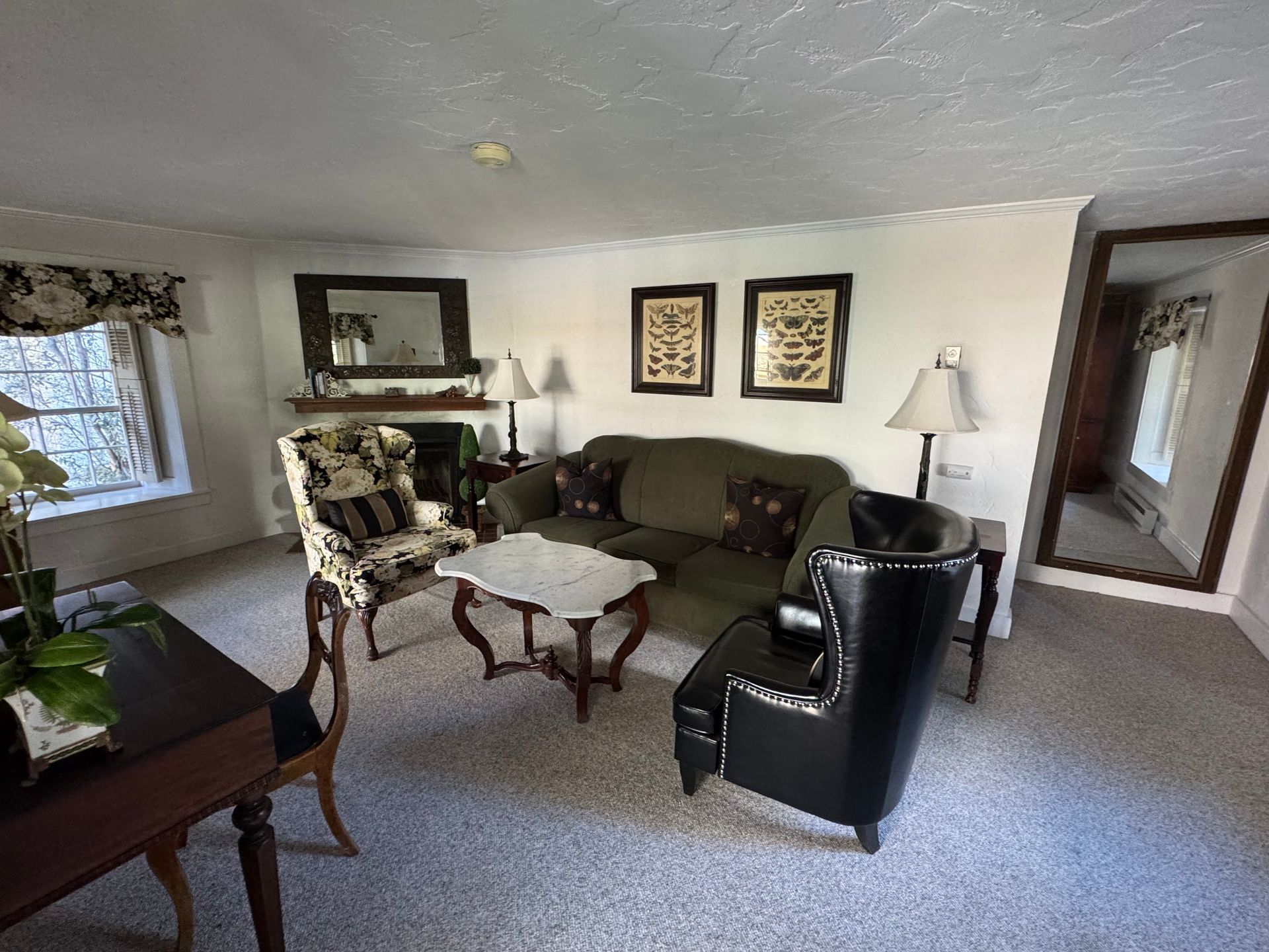 Living room with green sofa, two chairs, small table, mirror, artwork, and lamps.
