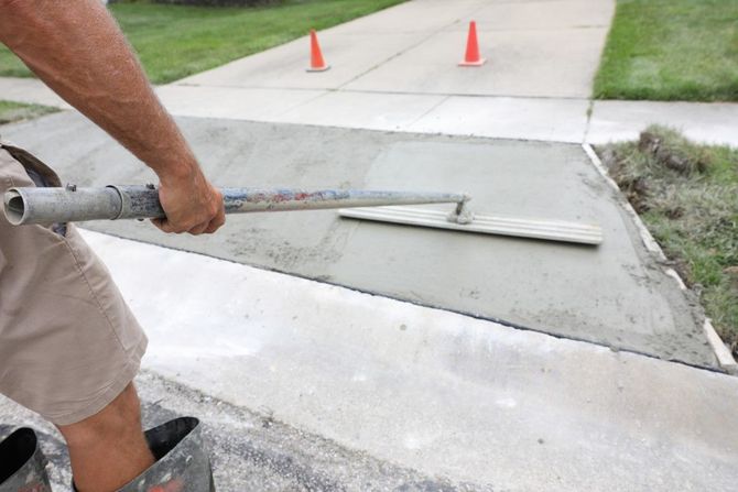 Worker smoothing fresh concrete on a sidewalk repair near orange traffic cones