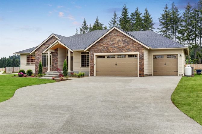 Single-story brick house with three-car garage and large concrete driveway, surrounded by lawn and trees