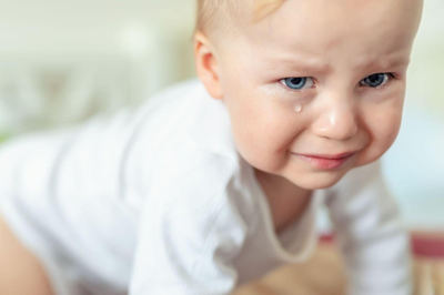 Crawling baby in a white shirt with a curious expression on a bed