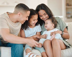 Family sitting together on a couch, smiling and holding a baby in a bright living room