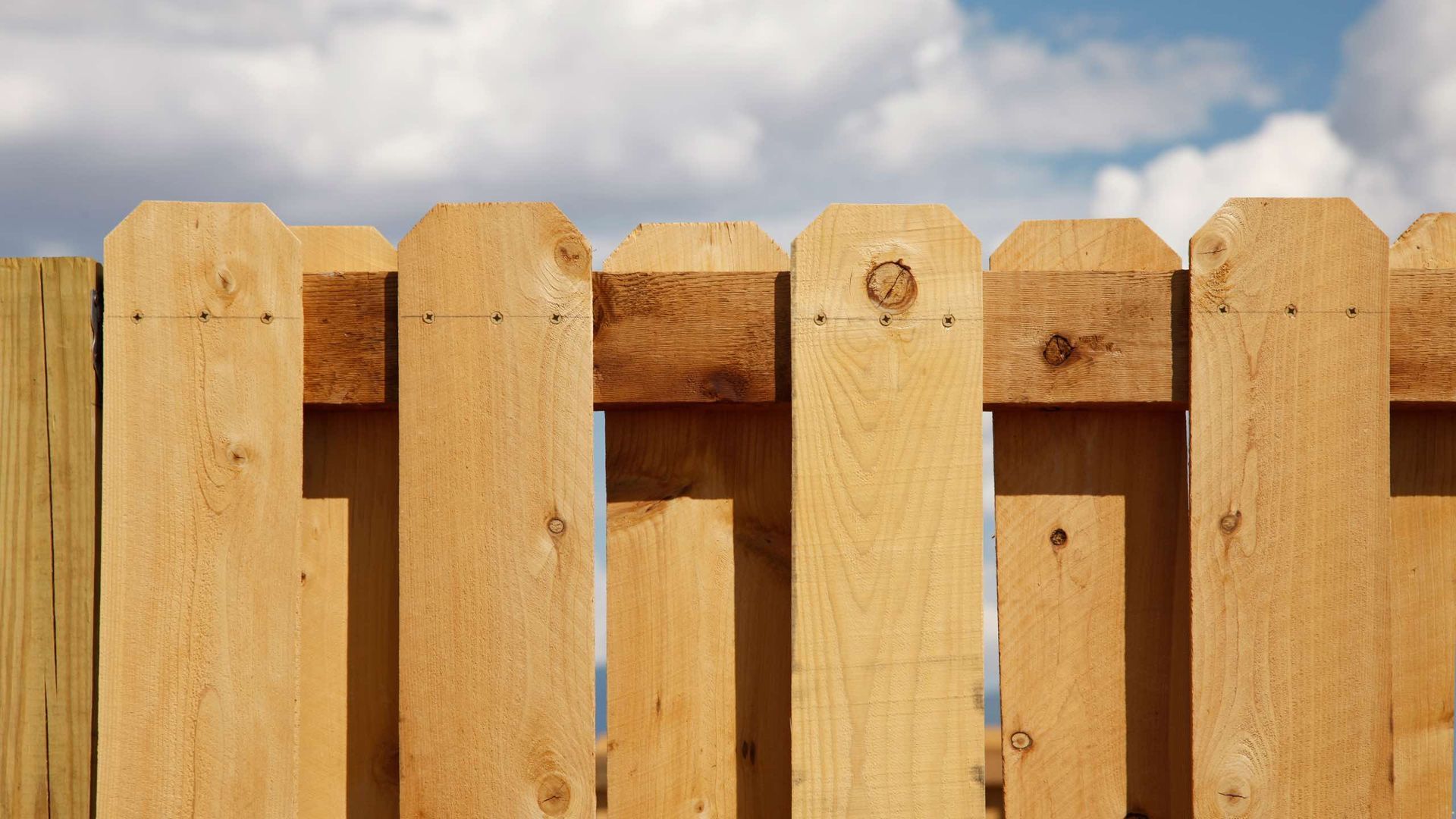 A wooden fence with a cloudy sky in the background.