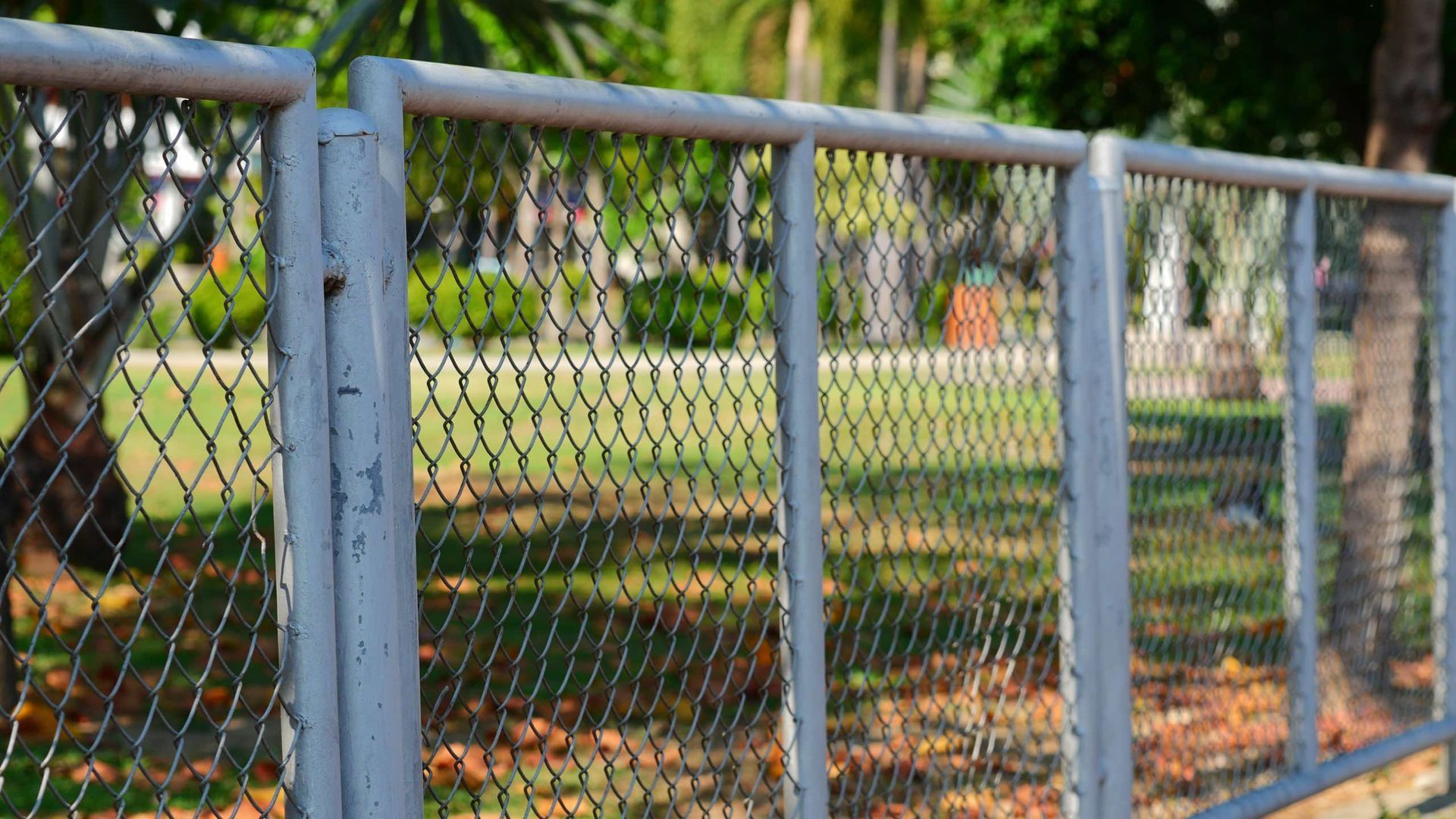 A chain link fence in a park with trees in the background.