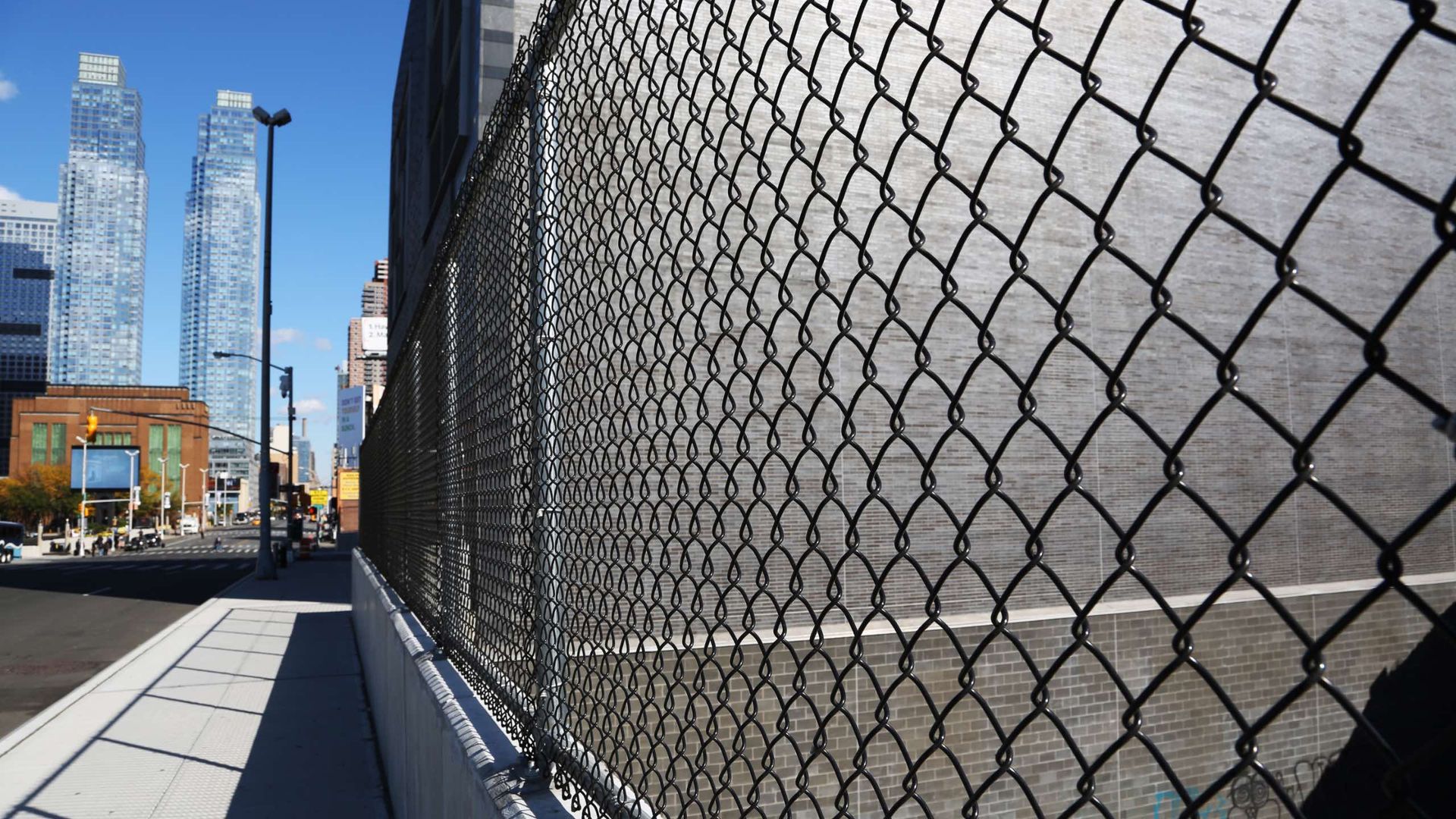 A chain link fence surrounds a basketball court in a city.