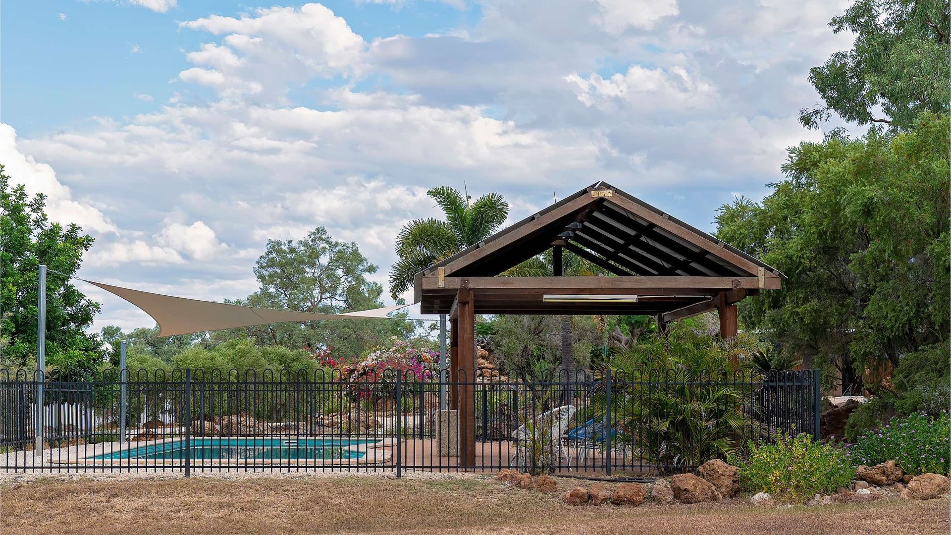 A wooden gazebo with a fence around it and a swimming pool in the background.