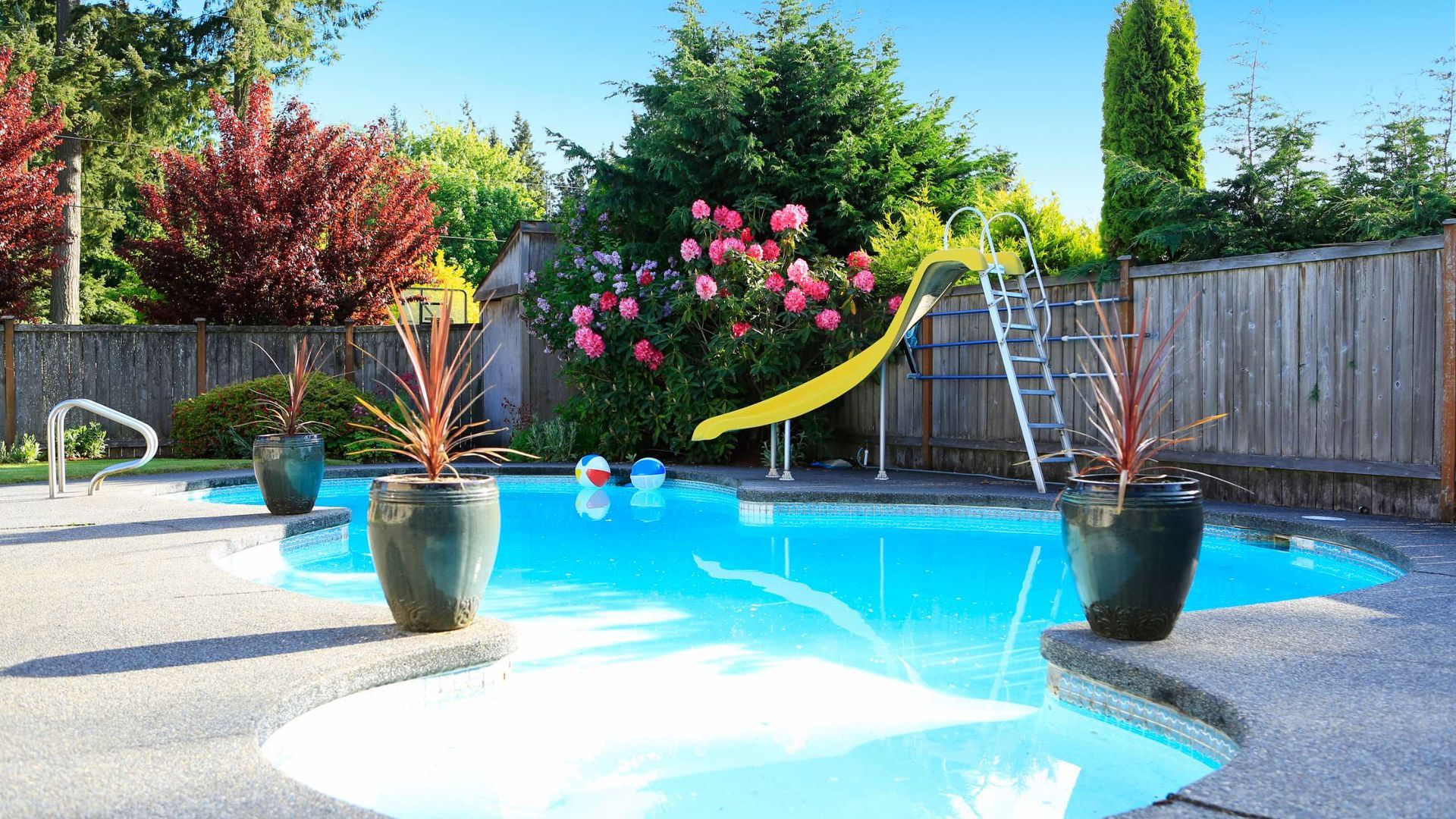 A swimming pool with potted plants and a slide in the backyard.