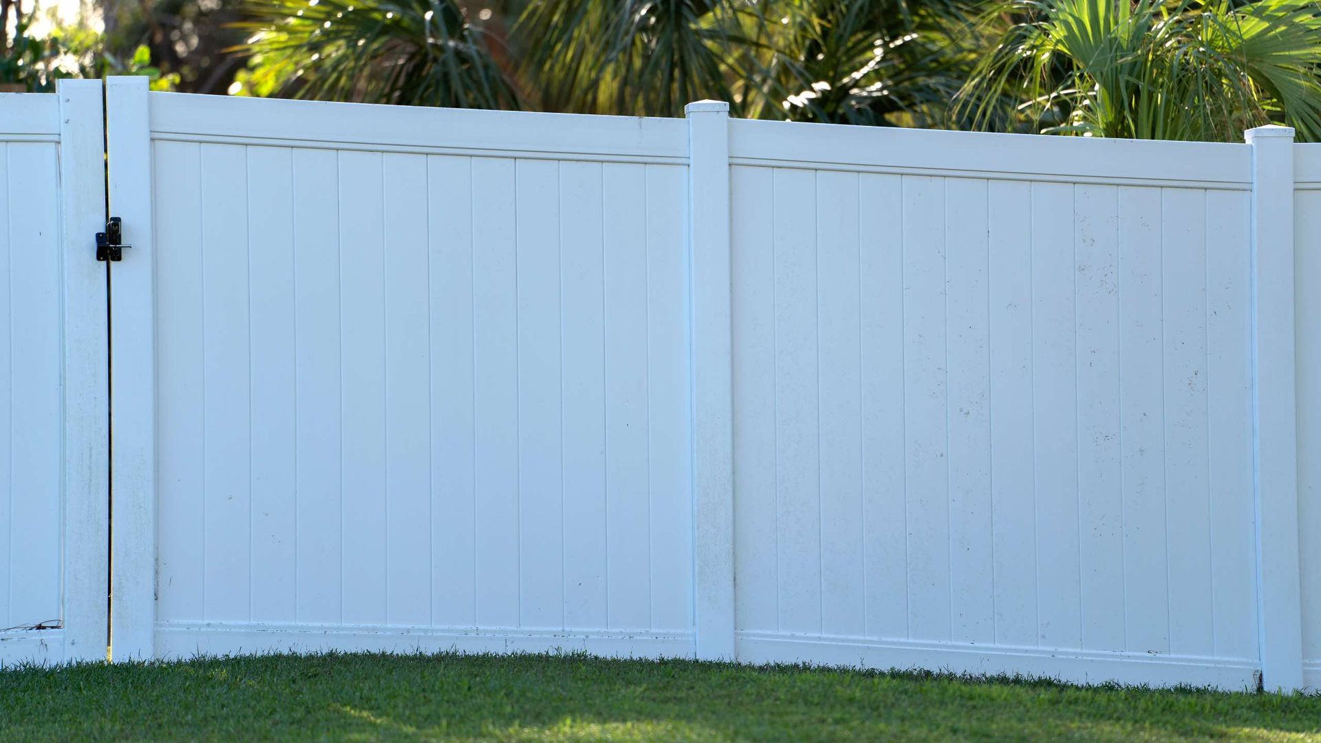 A white fence with a gate in the middle of a lush green yard.