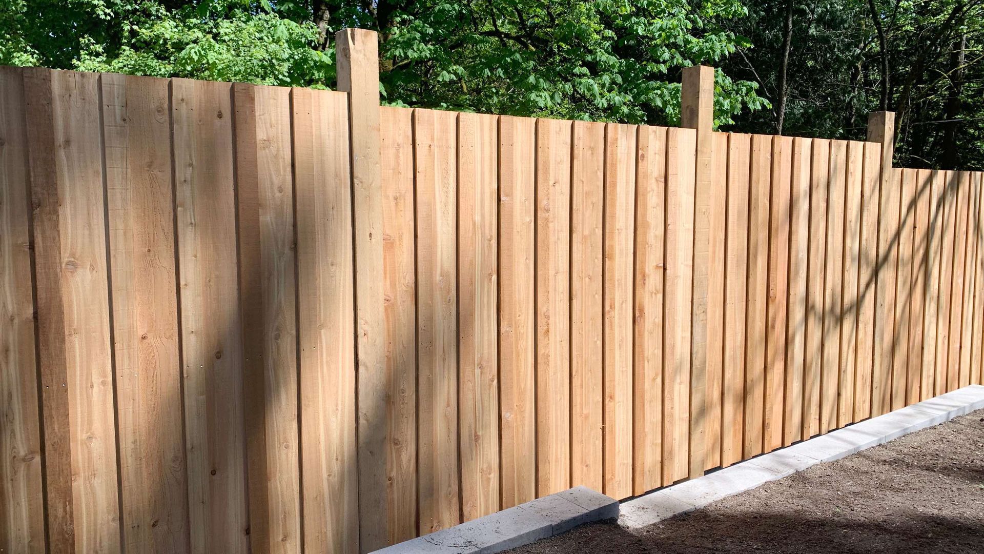 A wooden fence is surrounded by trees and gravel.