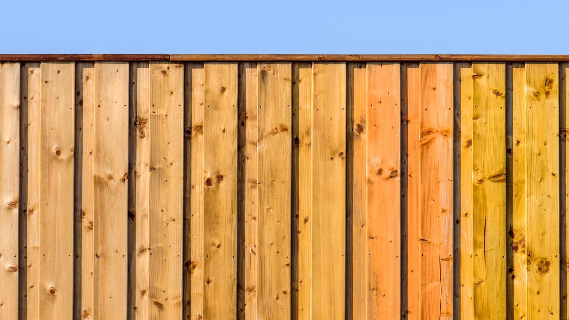 A close up of a wooden fence with a blue sky in the background.