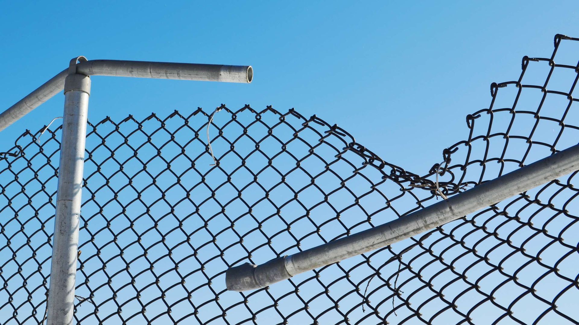 A broken chain link fence with a blue sky in the background