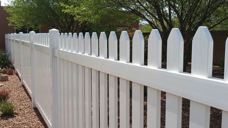 White picket fence in a yard with gravel and sparse landscaping.
