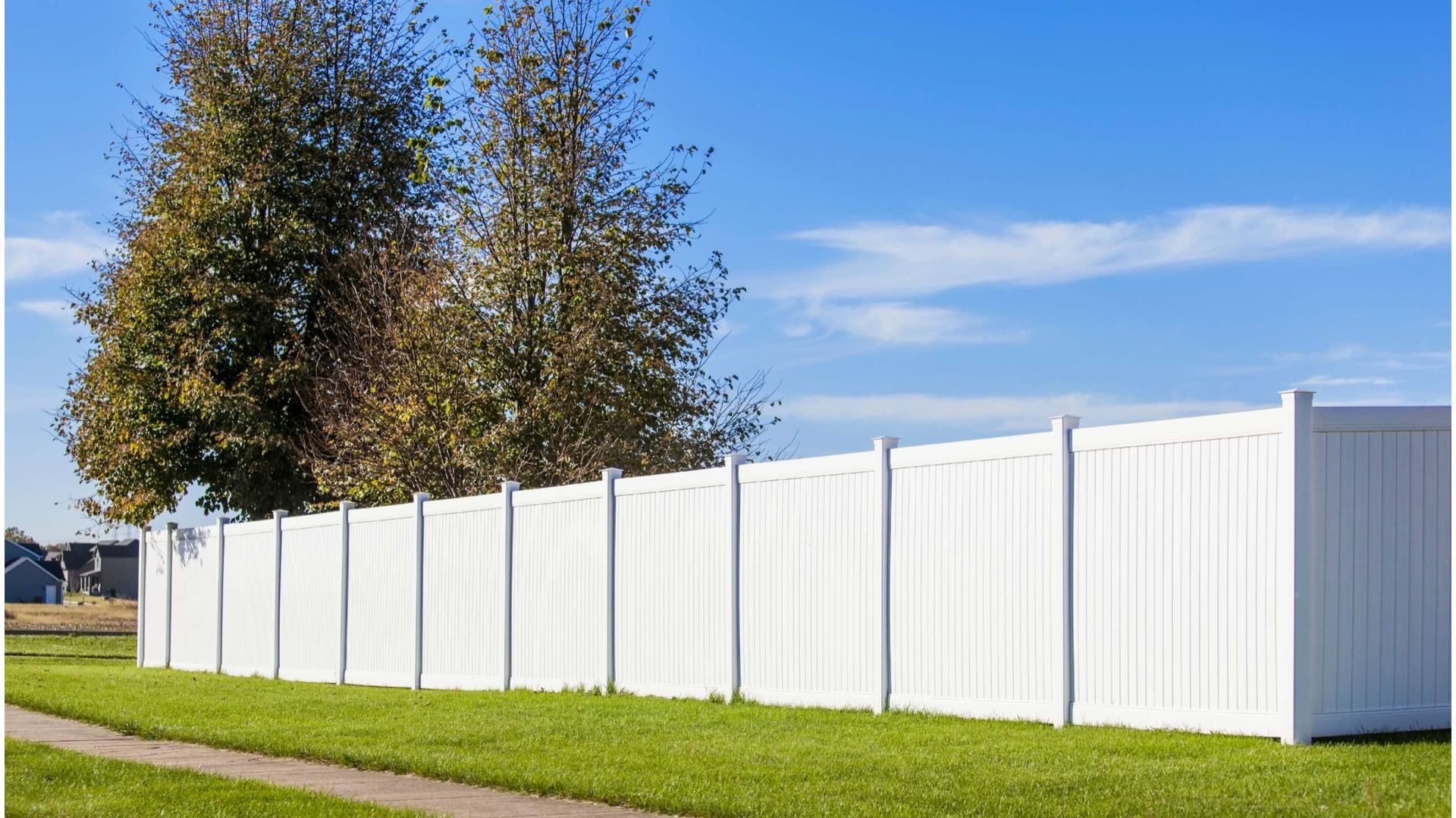 A white fence surrounds a lush green yard with trees in the background.