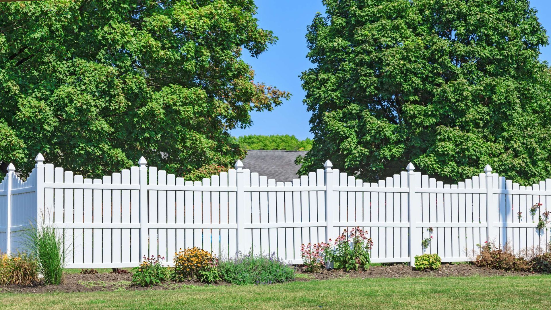 A white picket fence surrounds a lush green field with trees in the background.