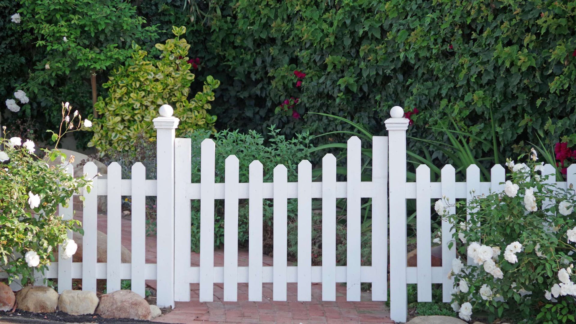 A white picket fence surrounds a lush green garden