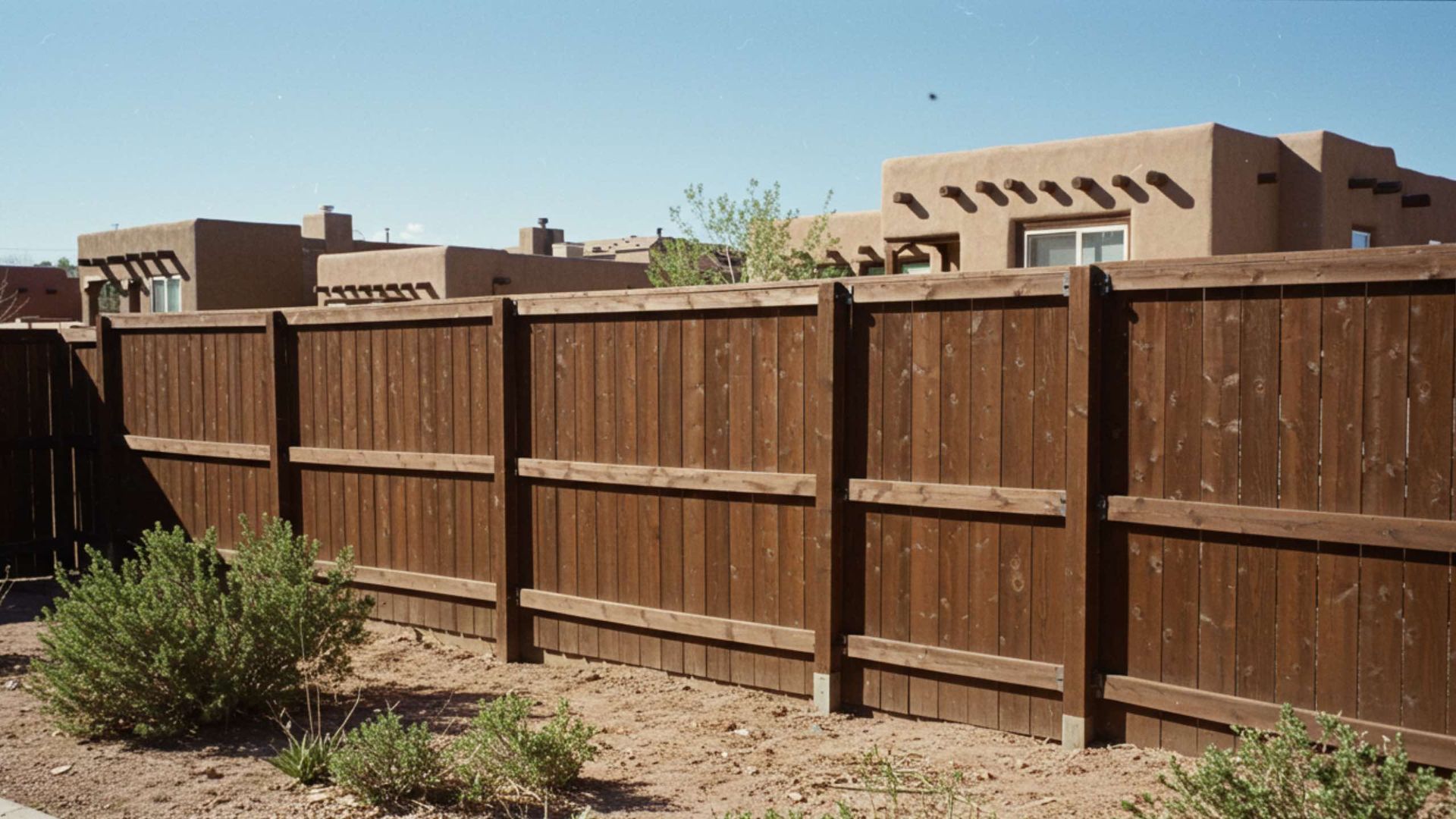 Wooden fence in front of Southwestern-style buildings under a blue sky.