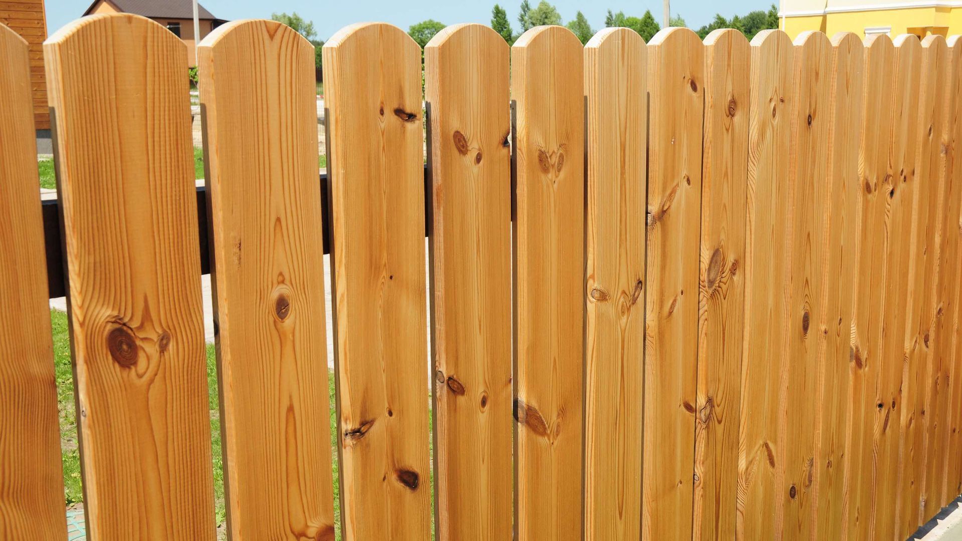 A close up of a wooden fence with a house in the background.