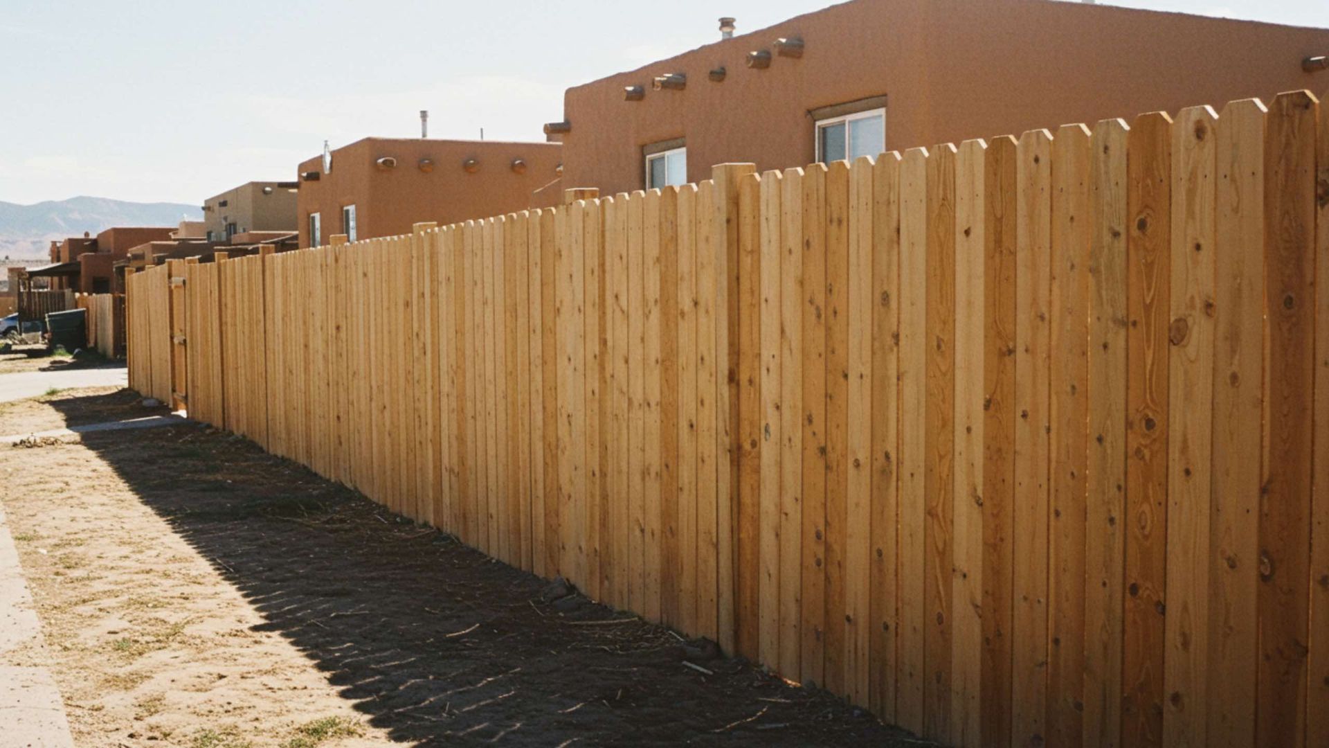 Wooden fence along a street, with buildings in the background. Sunny day.
