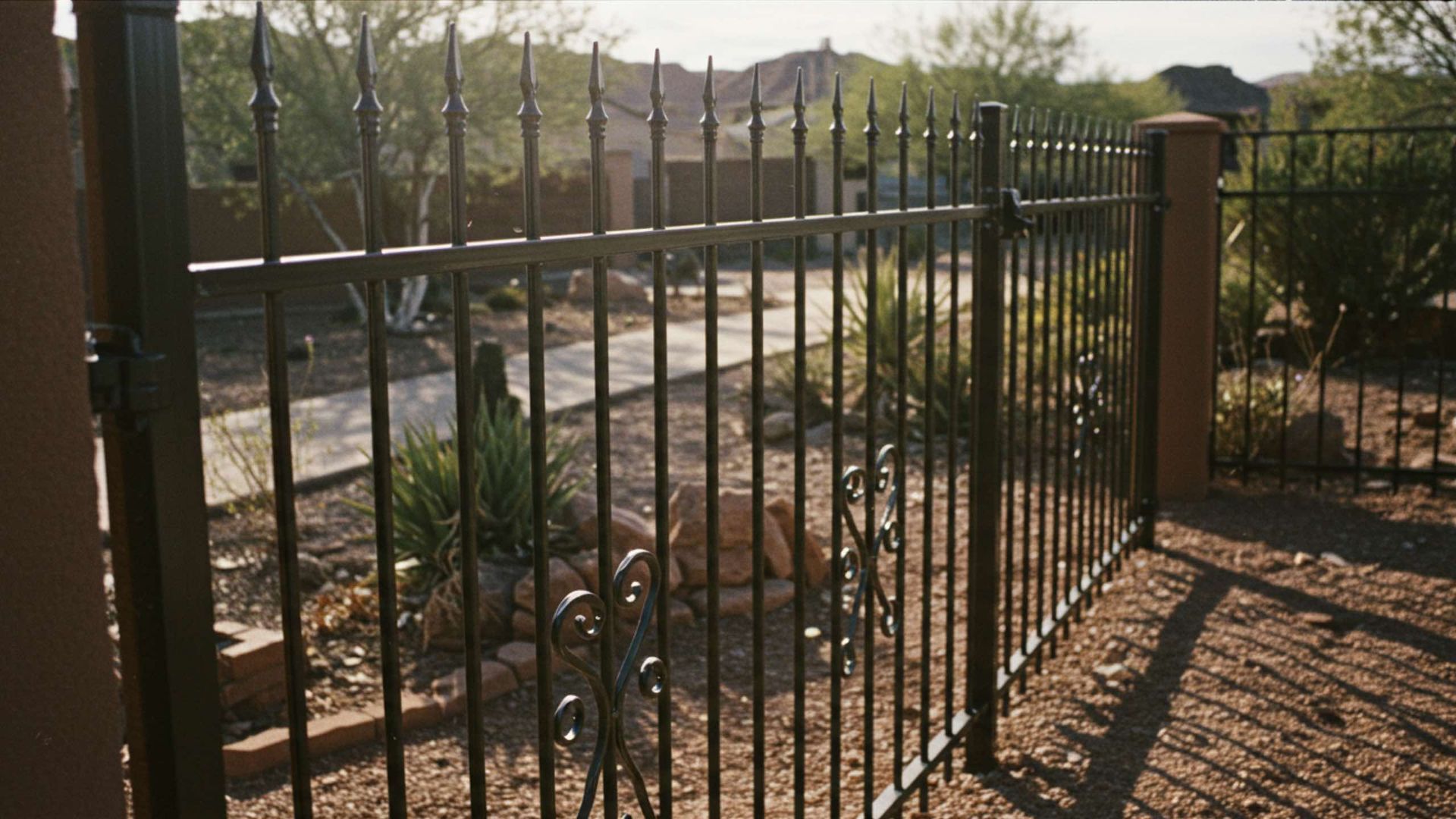 Black metal fence with decorative accents in a yard with gravel and desert plants.