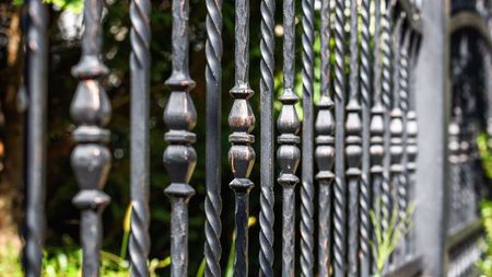 A close up of a wrought iron fence with a blurred background.