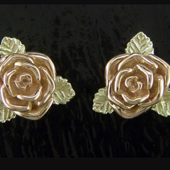 A pair of gold roses with green leaves on a black surface.