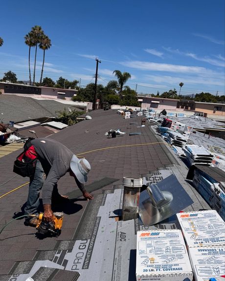 A roofer uses a nail gun to install shingles on a residential roof on a sunny day.
