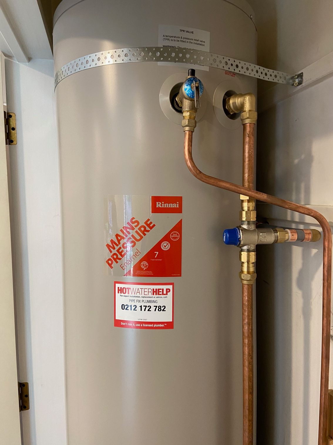 A tall, beige water heater with copper pipes and a red 